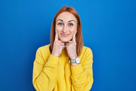 Téléchargez les photos : Young woman standing over blue background smiling with open mouth, fingers pointing and forcing cheerful smile - en image libre de droit