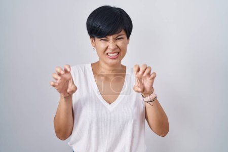 Téléchargez les photos : Jeune femme asiatique aux cheveux courts debout sur fond isolé souriant drôle faisant griffe geste comme chat, expression agressive et sexy - en image libre de droit