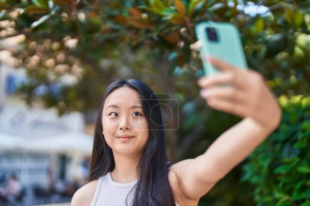 Foto de Joven mujer china sonriendo confiada haciendo selfie por el teléfono inteligente en el parque - Imagen libre de derechos
