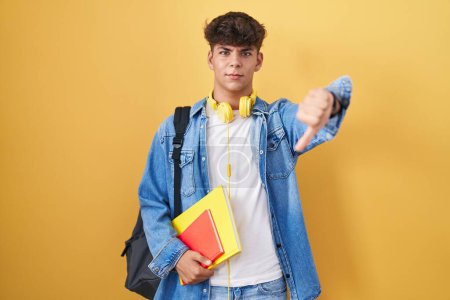 Photo for Hispanic teenager wearing student backpack and holding books looking unhappy and angry showing rejection and negative with thumbs down gesture. bad expression. - Royalty Free Image
