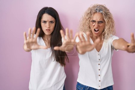 Photo for Mother and daughter standing together over pink background doing stop gesture with hands palms, angry and frustration expression - Royalty Free Image