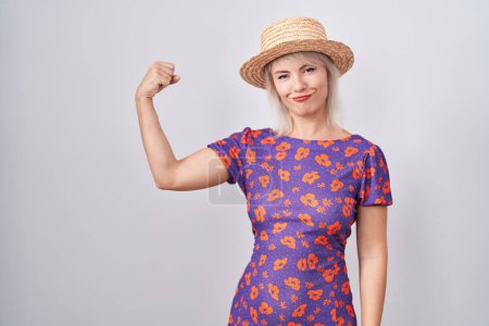 Téléchargez les photos : Jeune femme caucasienne portant des fleurs robe et chapeau d'été personne forte montrant muscle du bras, confiant et fier de la puissance - en image libre de droit