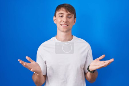 Photo for Caucasian blond man standing over blue background smiling cheerful offering hands giving assistance and acceptance. - Royalty Free Image