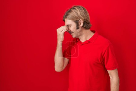 Foto de Hombre caucásico con bigote de pie sobre fondo rojo cansado frotando nariz y ojos sintiendo fatiga y dolor de cabeza. concepto de estrés y frustración. - Imagen libre de derechos