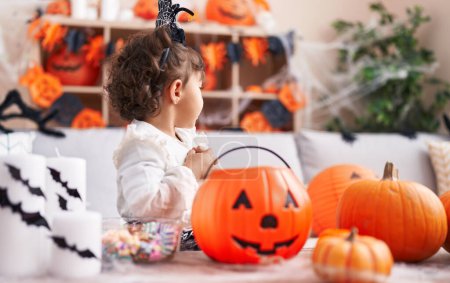 Photo for Adorable hispanic girl wearing halloween costume holding pumpkin basket at home - Royalty Free Image