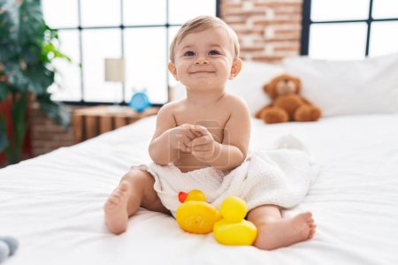 Téléchargez les photos : Adorable garçon caucasien assis sur le lit applaudissant les mains à la chambre - en image libre de droit