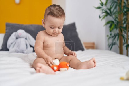 Foto de Adorable bebé caucásico jugando con juguete sentado en la cama en el dormitorio - Imagen libre de derechos