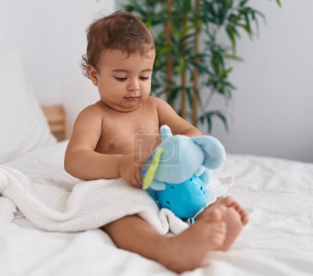 Photo for Adorable hispanic baby sitting on bed playing with elephant doll at bedroom - Royalty Free Image