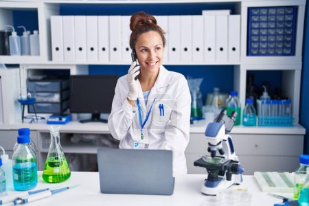 Photo for Young woman scientist talking on the smartphone using laptop at laboratory - Royalty Free Image