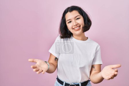 Téléchargez les photos : Jeune femme hispanique portant un t-shirt blanc décontracté sur fond rose souriant joyeuse offrant des mains donnant assistance et acceptation. - en image libre de droit