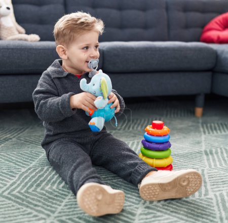 Foto de Adorable chico caucásico jugando con un juguete de elefante sentado en el suelo en casa - Imagen libre de derechos