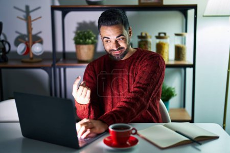 Photo for Young hispanic man with beard using computer laptop at night at home beckoning come here gesture with hand inviting welcoming happy and smiling - Royalty Free Image