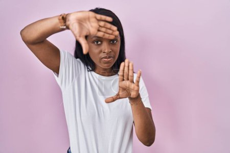 Téléchargez les photos : Jeune femme africaine portant casual t-shirt blanc faisant cadre en utilisant les mains paumes et les doigts, perspective de la caméra - en image libre de droit