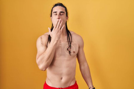 Photo for Hispanic man with long hair standing shirtless over yellow background bored yawning tired covering mouth with hand. restless and sleepiness. - Royalty Free Image