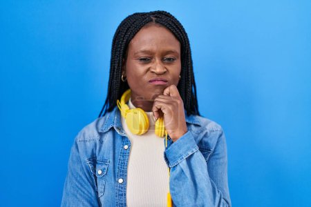 Foto de Mujer africana con trenzas de pie sobre fondo azul pensando concentrado en la duda con el dedo en la barbilla y mirando hacia arriba preguntándose - Imagen libre de derechos