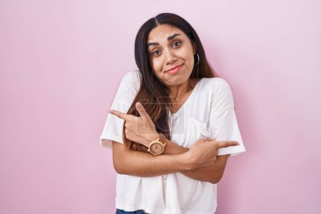 Téléchargez les photos : Jeune femme arabe debout sur fond rose pointant des deux côtés avec les doigts, direction différente en désaccord - en image libre de droit