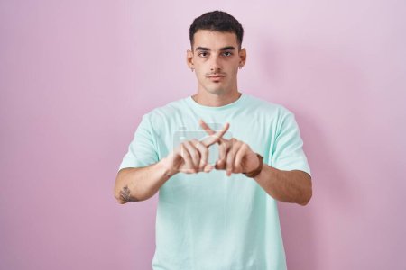 Téléchargez les photos : Bel homme hispanique debout sur fond rose expression de rejet croisant les doigts faisant signe négatif - en image libre de droit