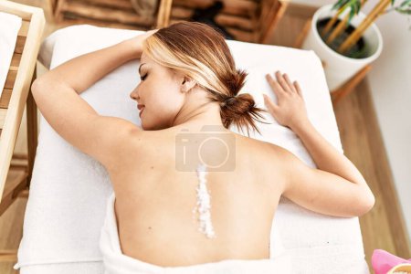 Foto de Young caucasian woman lying on table having back massage using salt at beauty salon - Imagen libre de derechos