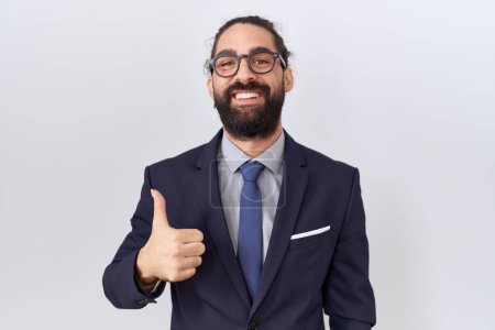 Foto de Hombre hispano con barba vistiendo traje y corbata haciendo un gesto feliz con la mano. aprobando la expresión mirando a la cámara mostrando éxito. - Imagen libre de derechos