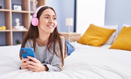 Téléchargez les photos : Jeune belle femme hispanique écoutant de la musique allongée sur le lit dans la chambre - en image libre de droit
