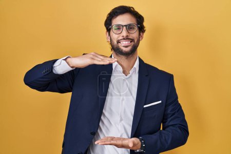 Photo for Handsome latin man standing over yellow background gesturing with hands showing big and large size sign, measure symbol. smiling looking at the camera. measuring concept. - Royalty Free Image
