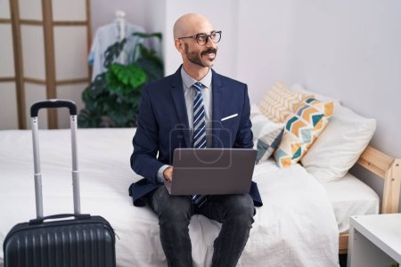 Téléchargez les photos : Jeune homme hispanique travailleur d'affaires en utilisant un ordinateur portable assis sur le lit à la chambre d'hôtel - en image libre de droit
