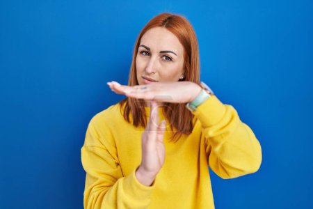 Foto de Young woman standing over blue background doing time out gesture with hands, frustrated and serious face - Imagen libre de derechos