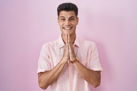 Photo for Young hispanic man standing over pink background praying with hands together asking for forgiveness smiling confident. - Royalty Free Image