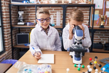 Photo for Adorable boys students using microscope writing notes at laboratory classroom - Royalty Free Image