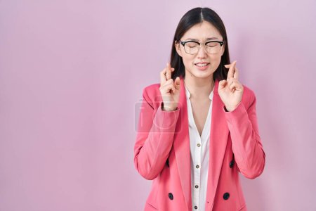 Téléchargez les photos : Entreprise chinoise jeune femme portant des lunettes geste doigt croisé sourire avec espoir et les yeux fermés. chance et concept superstitieux. - en image libre de droit