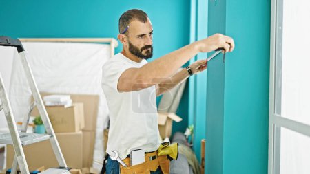 Photo for Young hispanic man repairman measuring wall at new home - Royalty Free Image