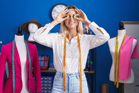 Téléchargez les photos : Young blonde woman tailor smiling confident holding buttons over eyes at tailor shop - en image libre de droit