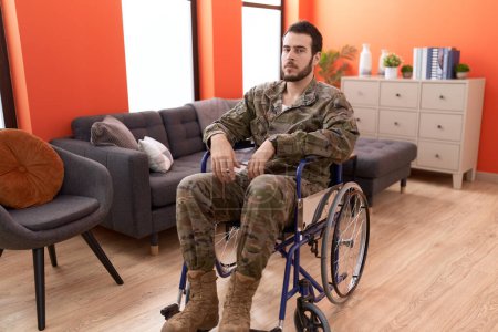 Foto de Joven soldado hispano herido sentado en silla de ruedas pensando actitud y expresión sobria buscando confianza en sí mismo - Imagen libre de derechos
