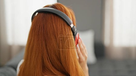 Téléchargez les photos : Jeune rousse femme écouter de la musique assis sur le canapé à la maison - en image libre de droit