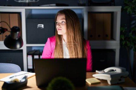 Téléchargez les photos : Jeune femme caucasienne travaillant au bureau la nuit regardant vers le côté, pose de profil relax avec visage naturel avec sourire confiant. - en image libre de droit