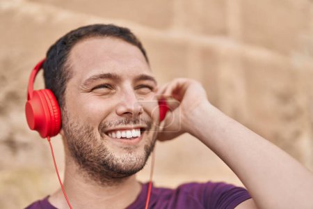 Téléchargez les photos : Jeune homme souriant confiant écoutant de la musique sur fond de briques isolées - en image libre de droit