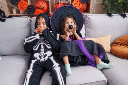 Foto de Adorable niño y niña con traje de halloween soplando globo en casa - Imagen libre de derechos