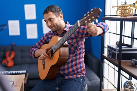 Foto de Joven músico sonriendo confiado tocando la guitarra clásica en el estudio de música - Imagen libre de derechos
