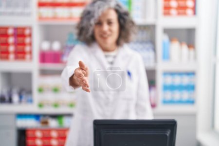 Téléchargez les photos : Middle age grey-haired woman pharmacist smiling confident shake hand at pharmacy - en image libre de droit