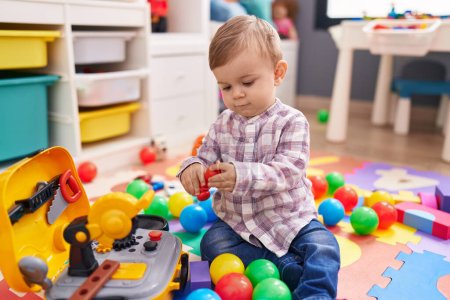 Photo for Adorable caucasian boy playing with balls sitting on floor at kindergarten - Royalty Free Image