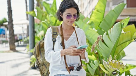 Téléchargez les photos : Jeune belle hispanique femme touriste en utilisant smartphone au parc - en image libre de droit