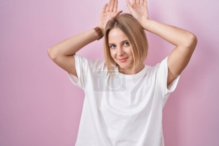 Téléchargez les photos : Young caucasian woman standing over pink background doing bunny ears gesture with hands palms looking cynical and skeptical. easter rabbit concept. - en image libre de droit