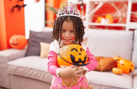 Foto de Chica afroamericana vistiendo traje de princesa sosteniendo cesta de calabaza en casa - Imagen libre de derechos