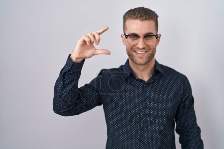 Photo for Young caucasian man standing over isolated background smiling and confident gesturing with hand doing small size sign with fingers looking and the camera. measure concept. - Royalty Free Image