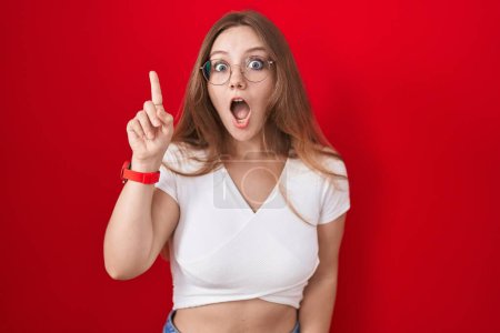 Téléchargez les photos : Jeune femme caucasienne debout sur fond rouge pointant du doigt avec une idée réussie. Sorti et heureux. numéro un. - en image libre de droit