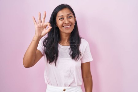Photo for Young hispanic woman standing over pink background smiling positive doing ok sign with hand and fingers. successful expression. - Royalty Free Image