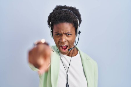 Foto de Mujer afroamericana con auriculares de agente de centro de llamadas apuntando disgustado y frustrado a la cámara, enojado y furioso con usted - Imagen libre de derechos