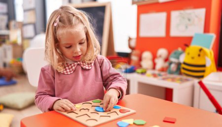 Foto de Adorable chica rubia jugando con matemáticas juego de puzzle en el jardín de infantes - Imagen libre de derechos