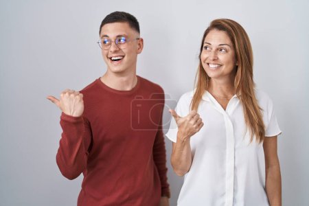 Photo for Mother and son standing together over isolated background smiling with happy face looking and pointing to the side with thumb up. - Royalty Free Image