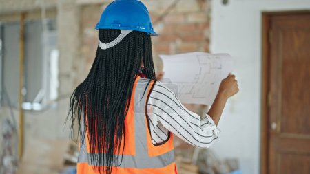 Photo for African american woman builder standing backwards reading house project at construction site - Royalty Free Image